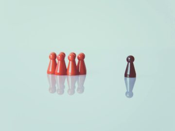 Red game pieces grouped with one isolated piece symbolizing social distancing on a reflective surface.
