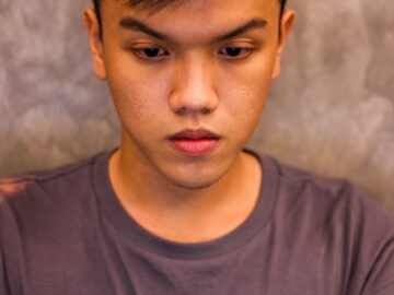 Teenage boy with dark hair focusing on a laptop screen indoors, captured in a vertical portrait.