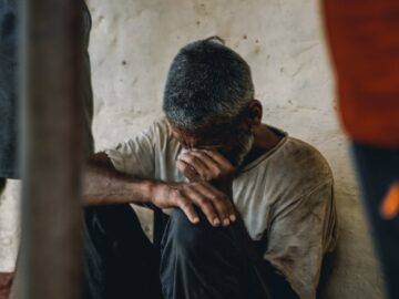 A senior adult man sits distraught indoors, conveying emotion and social issues.