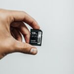 Close-up image of a hand holding a 128GB Lexar Professional SD card against a plain background.