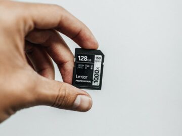 Close-up image of a hand holding a 128GB Lexar Professional SD card against a plain background.