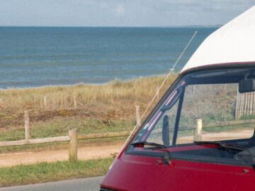 A vibrant red van parked on a coastal road with stunning sea views and clear skies.