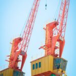 Two vibrant orange cranes under a clear blue sky, symbolizing modern industry and construction.