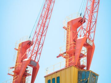 Two vibrant orange cranes under a clear blue sky, symbolizing modern industry and construction.