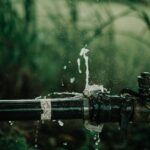 A detailed view of a leaking water pipe in a lush green garden setting.