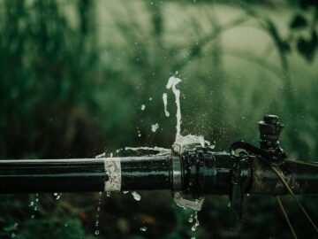 A detailed view of a leaking water pipe in a lush green garden setting.