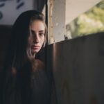 Moody portrait of a woman leaning against a wall in a dimly lit, abandoned building.