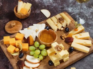 Gourmet cheese board with assorted cheeses, grapes, nuts, and a glass of wine on a rustic background.