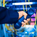 Close-up of a hand holding a telephone receiver in a server room emphasizing technology.