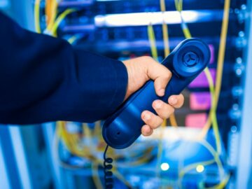 Close-up of a hand holding a telephone receiver in a server room emphasizing technology.