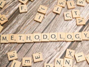 Wooden letter tiles spelling 'methodology' on a textured wooden surface, emphasizing research.