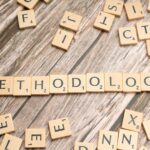 Wooden letter tiles spelling 'methodology' on a textured wooden surface, emphasizing research.