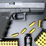 Top view of a Glock pistol, bullets, and flashlight on a black surface, showcasing firearms and ammunition.