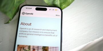 Close-up shot of a smartphone screen showing the OpenAI website with greenery in the background.