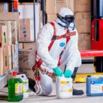 Industrial worker in protective gear handling chemicals in a warehouse environment.