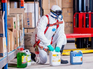 Industrial worker in protective gear handling chemicals in a warehouse environment.