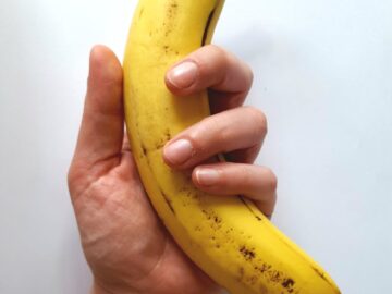 Close-up of a hand holding a ripe yellow banana against a white backdrop, showcasing freshness and tropical vibes.