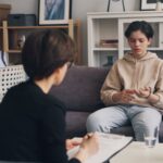 A teenager engages in a therapy session with a professional counselor in a modern office setting.