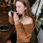 A young woman in casual wear sipping coffee in a cozy café setting, enjoying a peaceful moment.