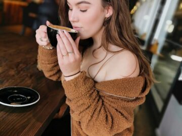 A young woman in casual wear sipping coffee in a cozy café setting, enjoying a peaceful moment.