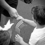 Black and white photo of a child receiving a small USA flag, symbolizing patriotism.