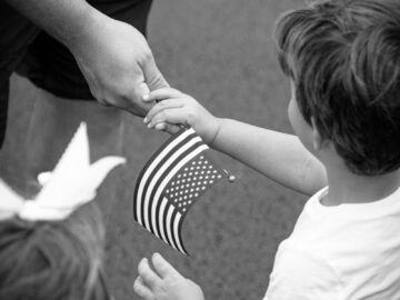 Black and white photo of a child receiving a small USA flag, symbolizing patriotism.