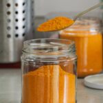 Close-up of bright turmeric powder in glass jars with spoon, enhancing culinary and health experiences.