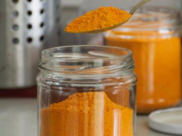 Close-up of bright turmeric powder in glass jars with spoon, enhancing culinary and health experiences.