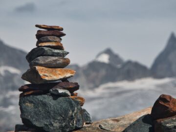 A balanced rock cairn on a rocky mountain with the Swiss Alps in the background.