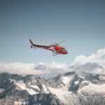 A vibrant red helicopter flies over the snowy peaks of the Swiss Alps, capturing a winter adventure.