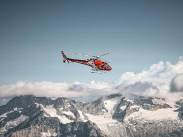 A vibrant red helicopter flies over the snowy peaks of the Swiss Alps, capturing a winter adventure.
