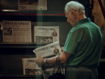 Senior adult browsing newspapers at a stand in São Paulo, Brazil. Captures urban life.
