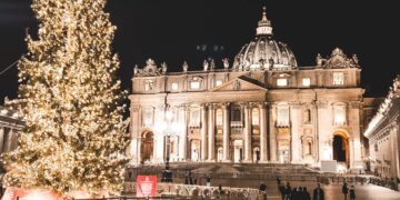 Illuminated St. Peter's Basilica and Christmas tree at night in Vatican City, showcasing festive holiday spirit.