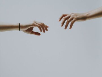 A minimalistic photo of two hands reaching out to each other against a soft, neutral background.