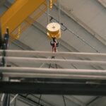 Close-up of an industrial crane hook lifting metal beams in a warehouse.
