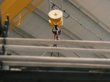 Close-up of an industrial crane hook lifting metal beams in a warehouse.