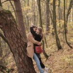 A couple lovingly embraces against a tree in a serene autumn forest setting.