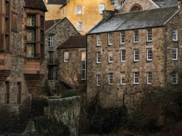 Charming view of historic stone buildings by a river in a quaint setting, showcasing architectural beauty.