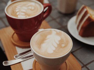 Delicious latte art accompanied by a slice of cake on a cafe table.