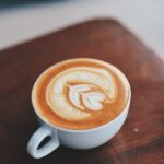 A beautifully crafted latte with intricate latte art inside a white ceramic cup on a wooden table.