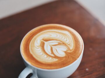 A beautifully crafted latte with intricate latte art inside a white ceramic cup on a wooden table.