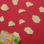 Delicious crispy potato chips scattered on a vibrant red background with packaging visible.