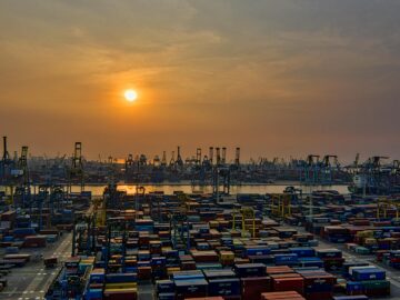 Sunset over a bustling seaport filled with stacked shipping containers and cranes.