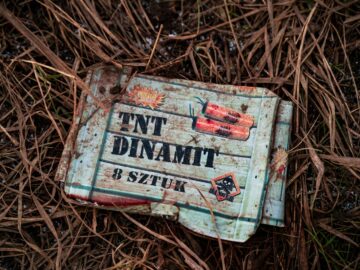 An old TNT box lies on dry grass, showcasing rustic and gritty textures outdoors.