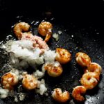 Close-up of sizzling shrimp and onions cooking in a pan, vibrant culinary scene.