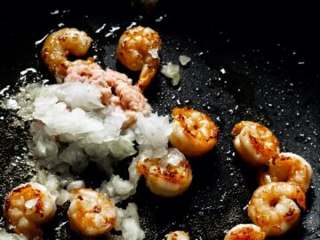 Close-up of sizzling shrimp and onions cooking in a pan, vibrant culinary scene.