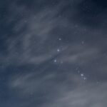 A serene night sky showcasing the Orion constellation amidst scattered clouds.