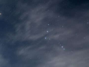 A serene night sky showcasing the Orion constellation amidst scattered clouds.