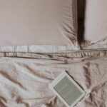 A minimalistic scene featuring an ebook reader on a neatly made bed with soft sheets and pillows.
