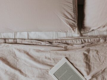A minimalistic scene featuring an ebook reader on a neatly made bed with soft sheets and pillows.